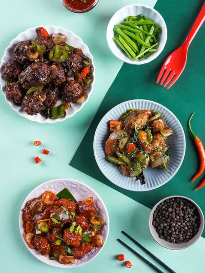 A flatlay of various Indo-Chinese appetizers like chili paneer and gobi manchurian. The geometric composition and color-blocked background create a modern and graphic visual.