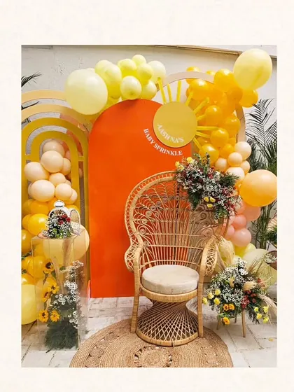 The main photo area for the 'Ray of Sunshine' baby shower, featuring a peacock chair, a backdrop of layered arches in sunset colors, and balloon garlands.