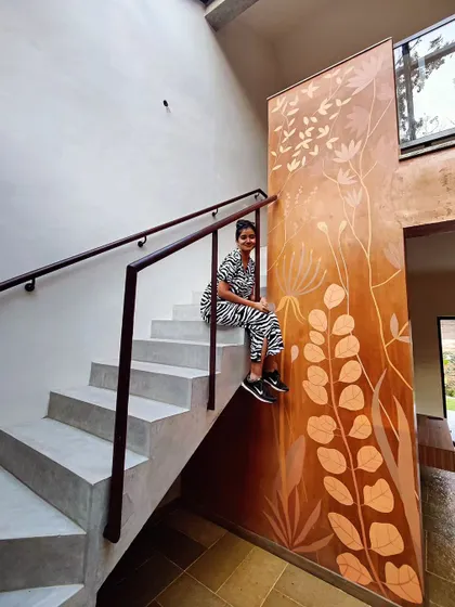 This mural flows up a tall staircase wall, with delicate wildflowers painted in light tones on a rich, textured terracotta surface.