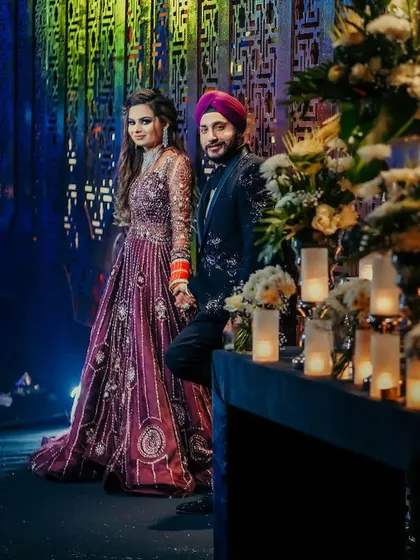 A stylish portrait of a Sikh couple at their reception. The groom's turban and the bride's embroidered gown are set against a backdrop of romantic candlelight, creating a moody and elegant atmosphere.