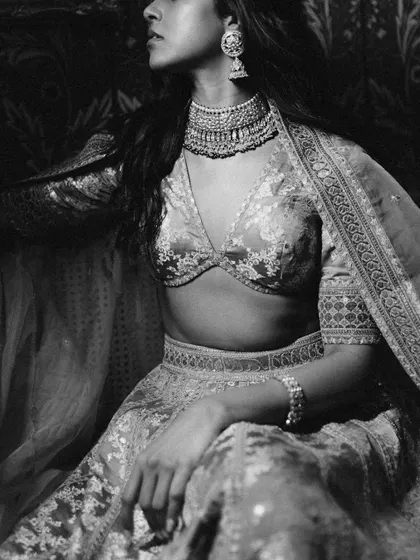 A moody and artistic black and white close-up of the bride. The lighting highlights the texture of her jewelry and the rich fabric of her Sabyasachi lehenga.