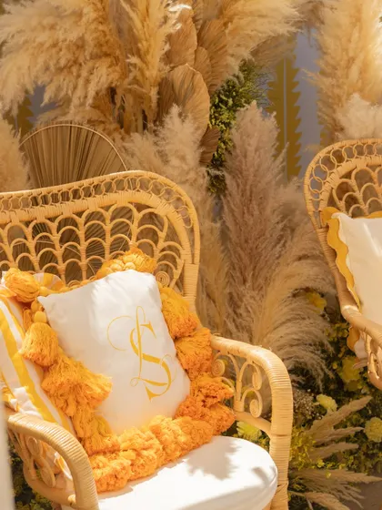 A close-up of the bride and groom's chairs, featuring custom pillows with their initials embroidered, surrounded by fluffy pampas grass.