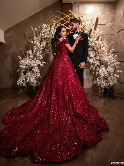 A dramatic, full-length portrait showcasing the bride's magnificent red reception gown. This is a true statement photograph.