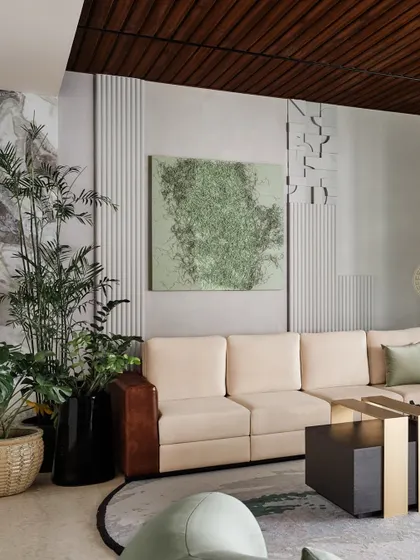 In this Bangalore home, the living area combines soft, neutral furniture with textured walls and a wooden ceiling. A large green artwork and lush plants add a touch of nature and color.