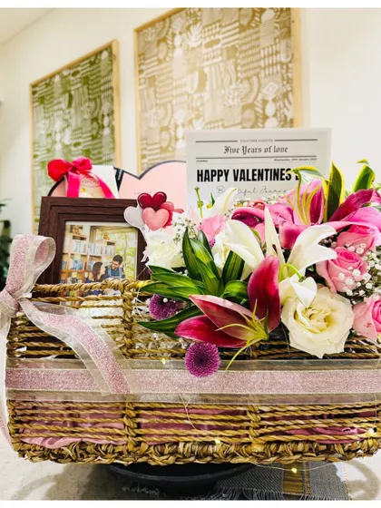 A beautiful Valentine's hamper for her, featuring a basket overflowing with fresh lilies, pink roses, and a custom 'Love Story' bath set.