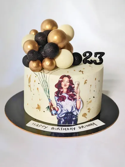 A fun and chic cake for a 23rd birthday. The design includes a trendy illustration, gold splatter, and a balloon-like cluster of black, white, and gold spheres.
