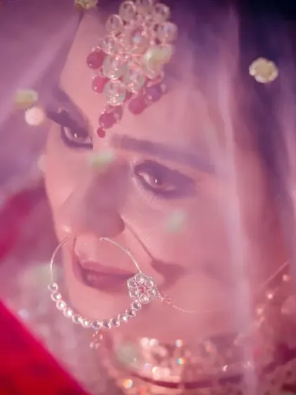 A beautiful, soft-focus shot of the bride looking through her veil. The purple and pink tones create a dreamy and romantic atmosphere.