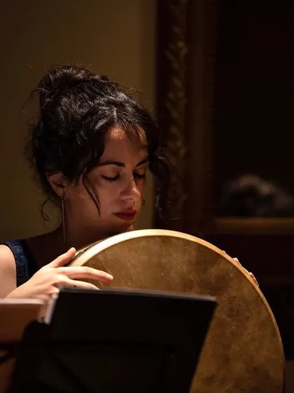 Our singer holding a frame drum, a percussion instrument found in many cultures. This image captures her serene expression as she contributes to the rhythmic and vocal harmony of the ensemble.