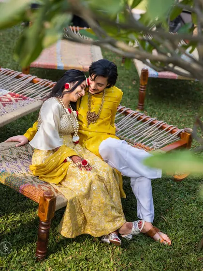A quiet, romantic moment during their Haldi ceremony. The couple, dressed in yellow, share a tender moment on a traditional charpai, surrounded by lush greenery.