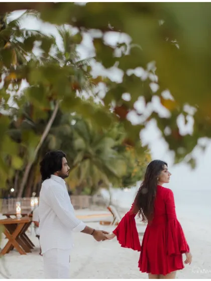 A candid moment of the couple walking hand-in-hand on a sandy beach, framed by lush tropical foliage. This shot feels natural and tells a story of a shared journey.