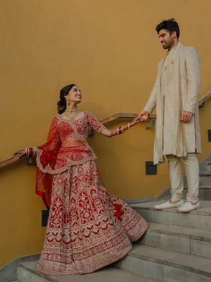 A regal portrait of the couple in their stunning red and cream wedding attire. We use architectural elements like staircases to add a touch of grandeur to our compositions.