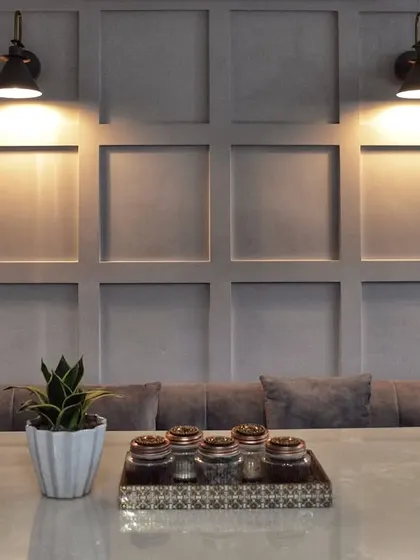 This dining nook features a comfortable built-in bench against a classic wainscoting wall, lit by industrial-style sconces for a cozy, cafe-like feel.