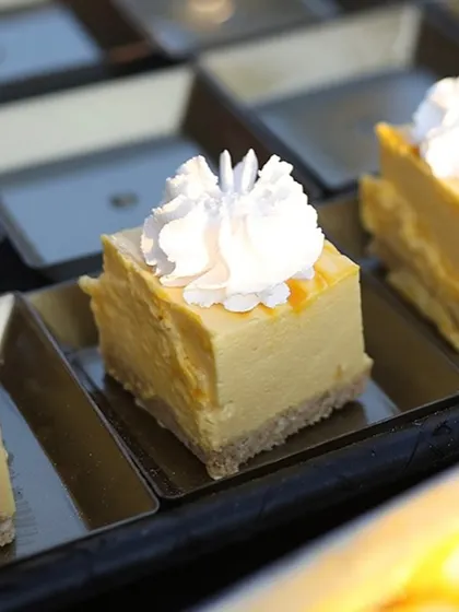 A close-up of a single bite of our creamy cheesecake. Topped with a delicate rosette of whipped cream, it's a perfect little morsel of happiness.