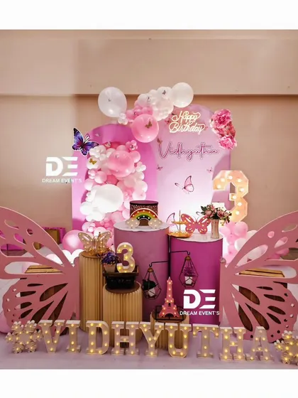 This whimsical butterfly-themed party features large, pink butterfly wing cutouts framing the dessert table, creating a perfect photo spot.