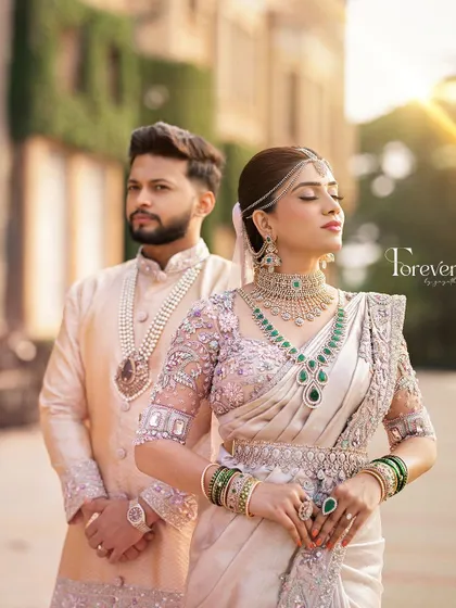 A regal portrait of the couple. The groom's pastel sherwani with a matching dhoti is adorned with a pearl necklace, creating a look of modern royalty against the palace backdrop.