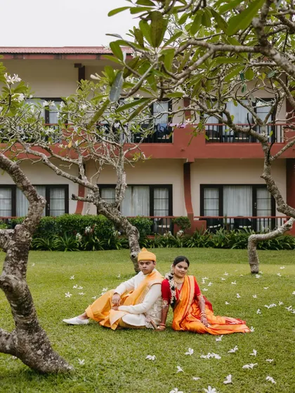 A serene portrait of a couple sitting together on the grass under a frangipani tree, sharing a quiet moment amidst nature.