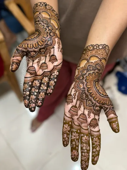 This angle highlights the hanging jhumka motifs on the palm, a playful and traditional element in bridal mehendi. The design is filled with delicate lotus flowers and fine line work.
