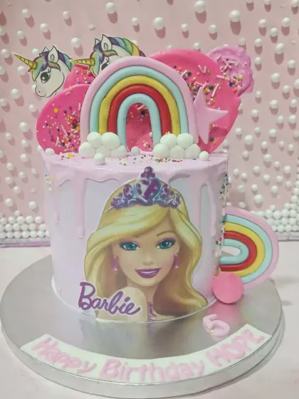 A fun and colorful Barbie-themed drip cake. This pink cake is decorated with rainbows, unicorns, and a Barbie illustration for a magical celebration.