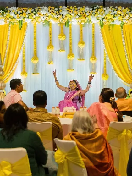 The bride takes center stage, celebrating with her guests during her haldi ceremony, set against a bright yellow backdrop.