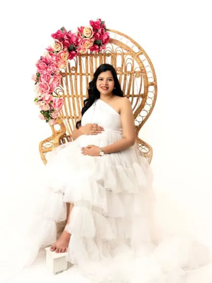 Seated on a peacock chair, this mom-to-be is the picture of serenity and grace in a beautiful white ruffled gown.