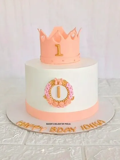 A royal first birthday cake for a little princess. This simple yet elegant design features a beautiful pink crown topper and a floral wreath monogram.