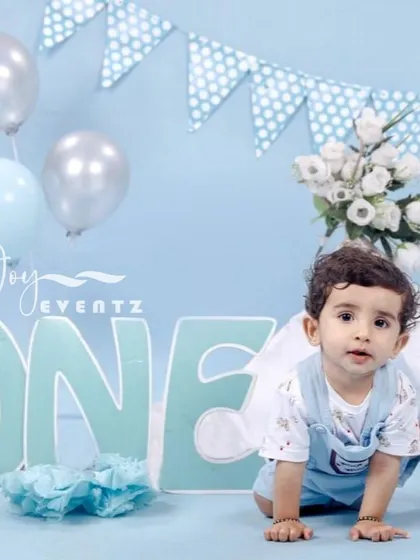 A classic blue-themed cake smash for a baby boy turning one. The set features a large "ONE" sign, blue and silver balloons, and polka dot bunting, providing a perfect backdrop for this milestone moment.