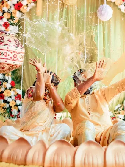 A creative shot of a couple being drenched with water during their Haldi. The unique lotus-shaped tub adds a special touch to the celebration.