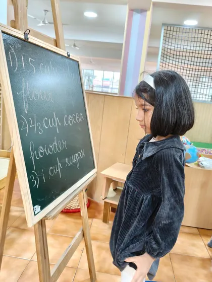 A child carefully reads the recipe on the chalkboard before starting to bake. This shows how we integrate literacy into practical, everyday activities, making learning meaningful.