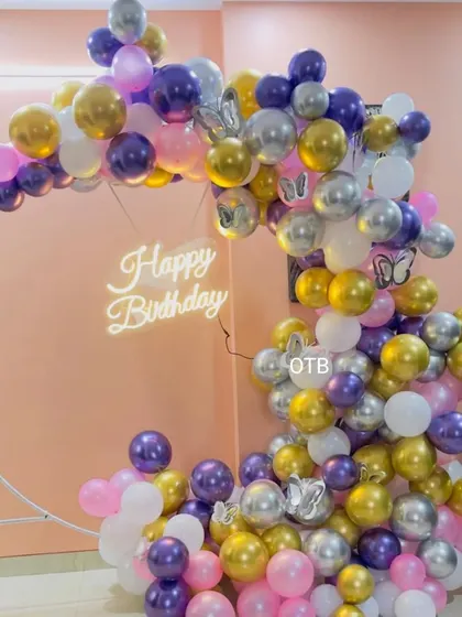 A whimsical and colorful balloon ring arrangement. The mix of purple, pink, gold, and silver balloons with butterfly accents creates a playful and dreamy vibe.