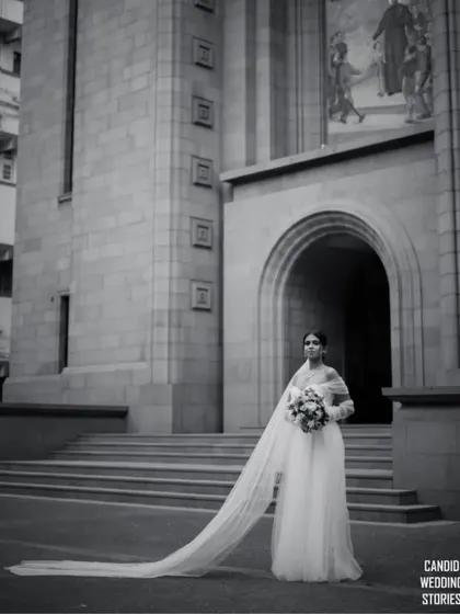 The timeless elegance of a bride. This portrait, shot in classic black and white, highlights the serene beauty and anticipation before the ceremony, showcasing our artistic approach to bridal photography against a stunning architectural backdrop.