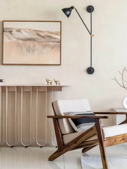 A cozy reading corner featuring a unique console table with curved metal legs. The design pairs a comfortable wooden armchair with an adjustable wall lamp, creating a perfect spot for relaxation.