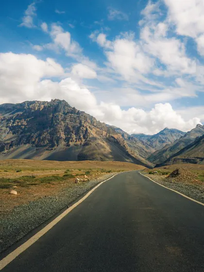 An empty road stretching through the vast, arid landscape of Spiti Valley. This classic road trip shot evokes a sense of adventure and freedom.