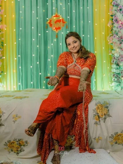 The bride showing off her beautiful Mehendi-adorned hands during her pre-wedding ceremony, looking playful and happy.