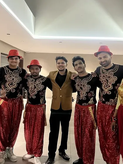 Our team of male and female dancers in vibrant red and yellow folk-inspired costumes, posing with our lead choreographer backstage before a performance.