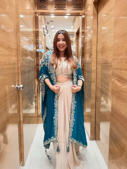 Don’t just stand out, stand in style with this dhoti and cape set. The teal embroidered cape adds a pop of color to the elegant beige dhoti pants and crop top.
