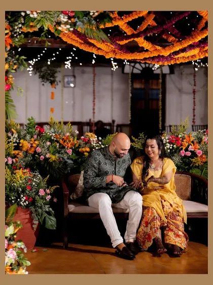 A candid moment of laughter and joy between the couple at their colorful Mehendi ceremony. The rich floral decor and warm lighting create an intimate and happy setting.