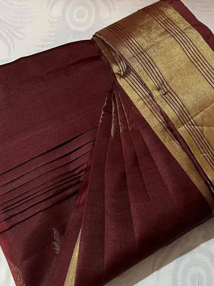 A simple and elegant maroon saree with a gold striped border, perfectly pleated for a formal or work occasion.