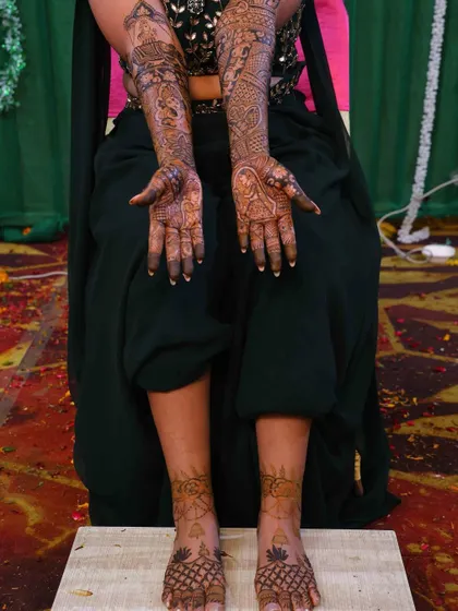 A complete bridal look, showing the intricate mehndi on both hands and feet. The feet feature a simple yet elegant design that complements the heavy work on the arms.