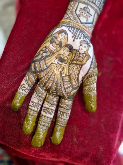 The fresh henna paste shows the intricacy of the family portrait. The names of the bride's 'aai-baba', 'didi', and 'masi' are clearly written on her fingers.