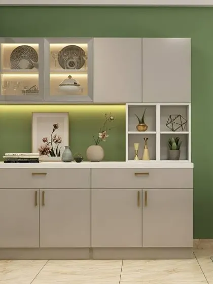 A charming crockery unit in a soft grey finish with a sage green accent wall. The design includes glass-door cabinets on top and open cube shelving for displaying small plants and decor.