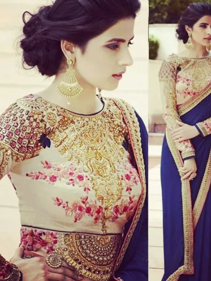 This boat-neck blouse features heavy gold embroidery around the neckline and floral patterns on the body. It's a statement piece that can elevate a simple saree.