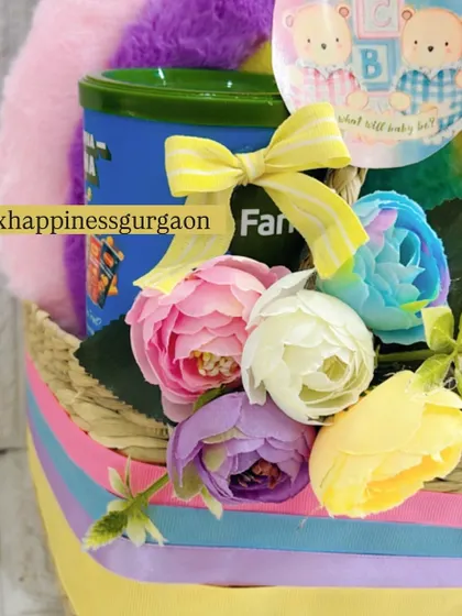 A close-up of the rainbow-themed hamper, highlighting the colorful artificial flowers and the "What will baby be?" tag, adding to the fun and anticipation of a baby shower.