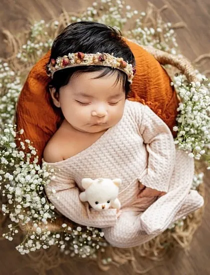 A peaceful newborn nestled in a rustic basket, surrounded by baby's breath and holding a tiny teddy. These posed shots are perfect for capturing their angelic features.