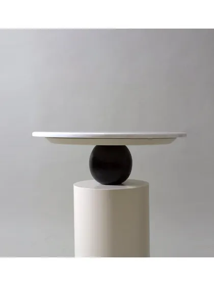 This unique coffee table features a marble top perched on a sculptural base, combining a wooden sphere and a cylindrical pedestal. It's a piece of functional art.