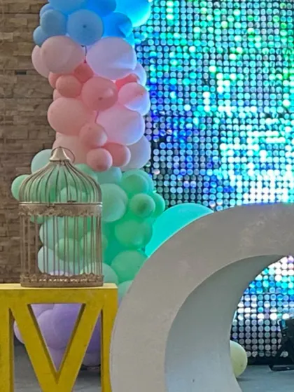 A detail shot of a party corner, showing a crescent moon prop and a decorative birdcage next to a shimmer wall and pastel balloons.