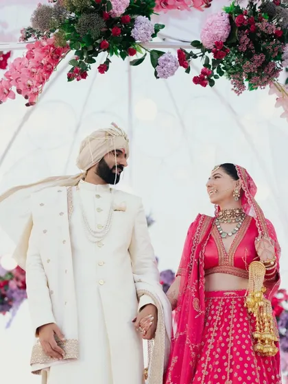 A beautiful moment between a couple under their beachside mandap in Abu Dhabi. The vibrant pink of the bride's lehenga stands out against the sea and sky.