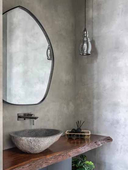 The powder bathroom combines the raw beauty of concrete walls with the organic warmth of a live-edge wood counter. A natural stone sink and a simple pendant light complete this study in texture and minimalism.
