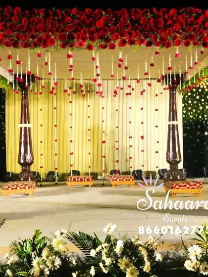 A magnificent wedding mandap with a canopy of red roses and hanging floral strings. The dark wooden pillars provide a rich contrast, creating a look of timeless grandeur for the ceremony.