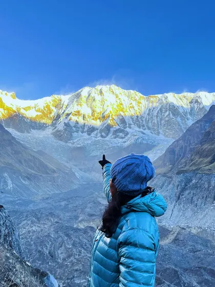 A trekker points towards the sunlit peaks of the Annapurna range at sunrise. Reaching the base camp to witness this moment is the ultimate reward.