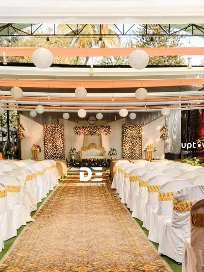 An outdoor wedding setup with elegant chair covers and an aisle runner.